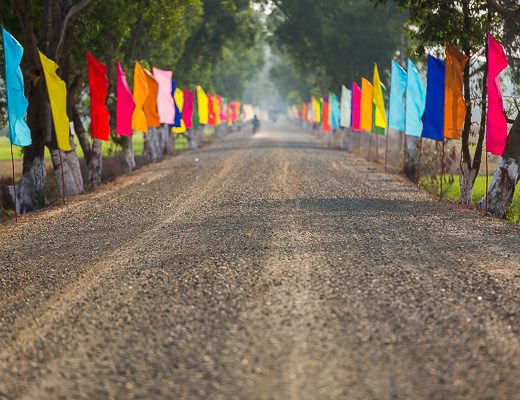 Lush greenery and blue skies are typically complemented by colorful clothing, buildings, and places of worship. These flags were lining the road to a new temple outside Kampong Chhnang, Cambodia.